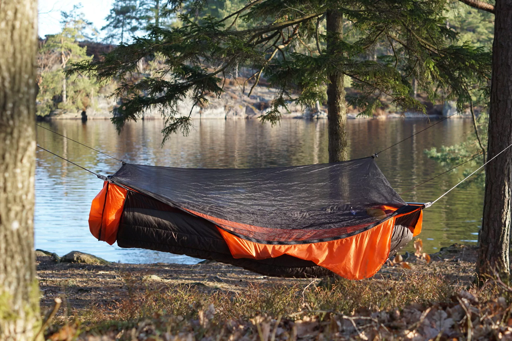 an orange ridgerunner hammock with a black lynx underquilt hanging near a lake